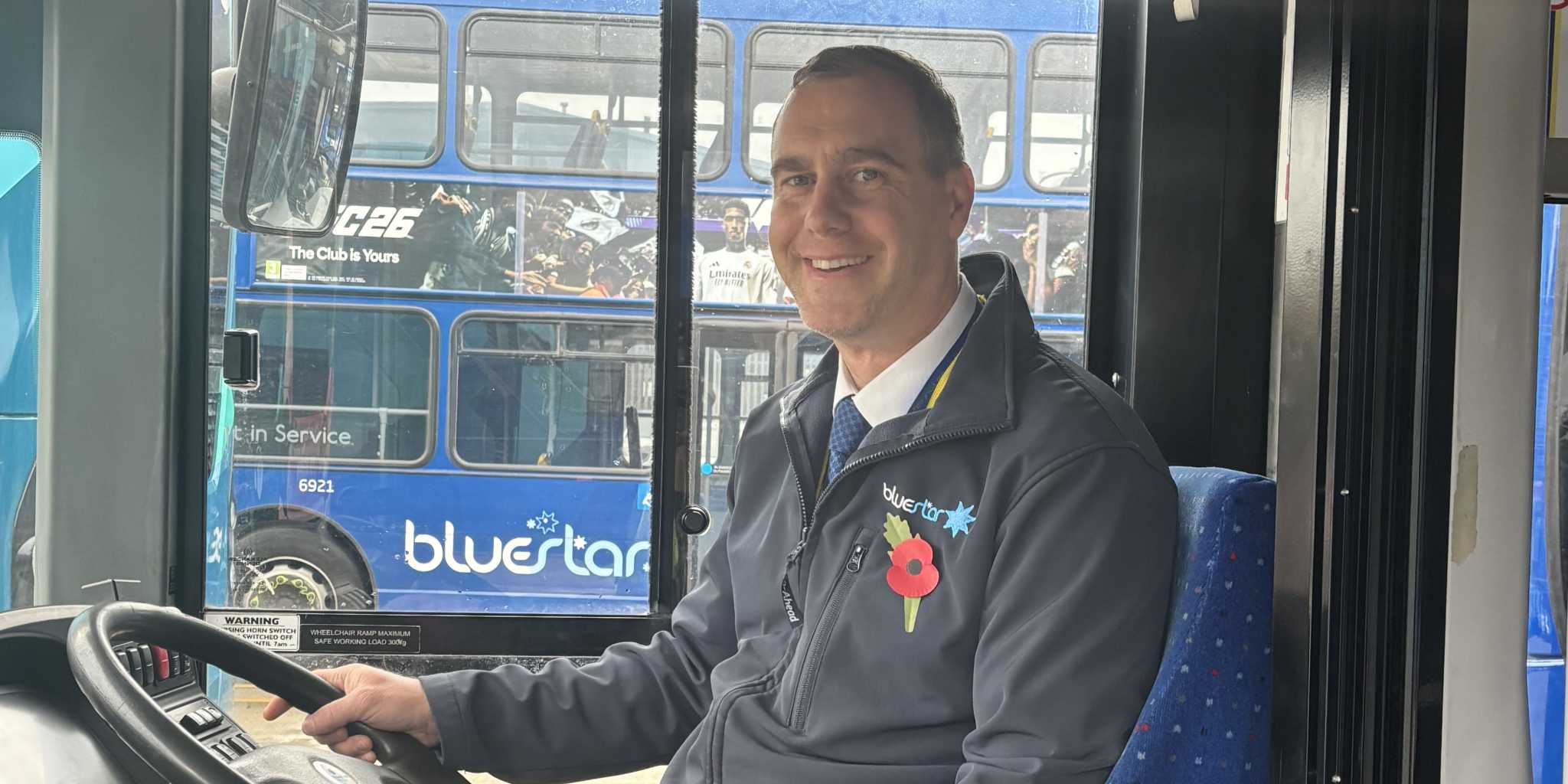 Bluestar bus driver in the cab wearing a poppy